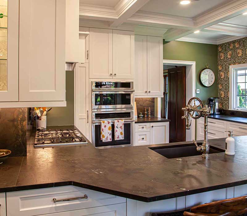 A chrome pull-down wheel faucet is the centerpiece of this traditional kitchen with natural slate countertops, art nouveau floral wallpaper, and green walls.