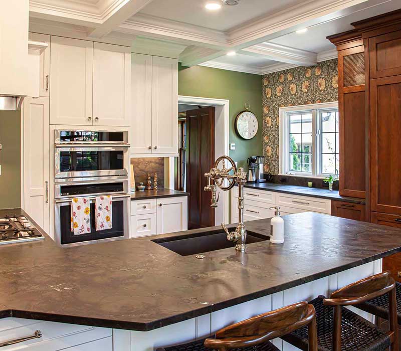 A chrome pull-down wheel faucet is the centerpiece of this traditional kitchen with natural slate countertops, art nouveau floral wallpaper, and green walls.