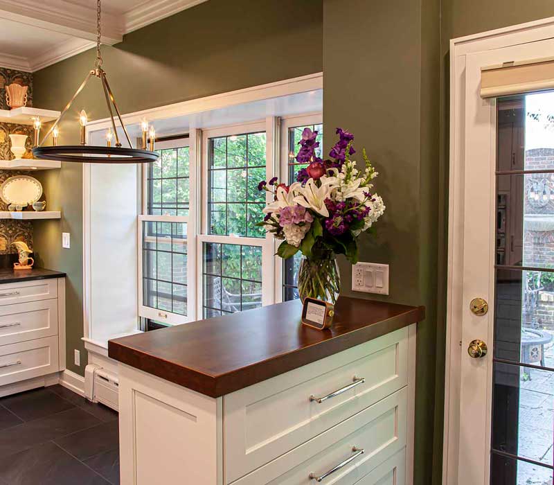 A chrome pull-down wheel faucet is the centerpiece of this traditional kitchen with natural slate countertops, art nouveau floral wallpaper, and green walls.