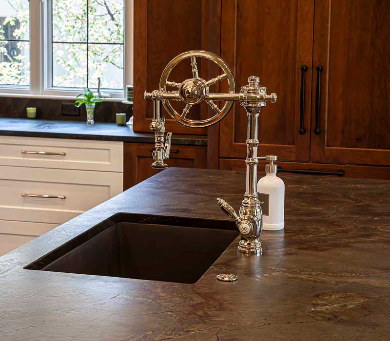 A chrome pull-down wheel faucet is the centerpiece of this traditional kitchen with natural slate countertops, art nouveau floral wallpaper, and green walls.