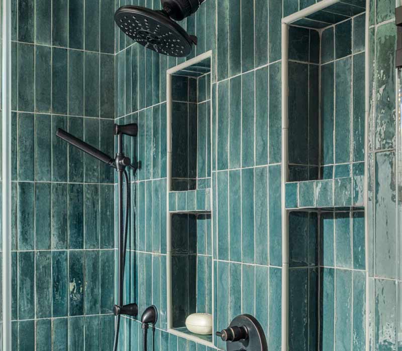 This whole-house remodel features a prairie-style kitchen adorned with custom cabinetry by DHDK, a primary suite with custom alder armoire, and bathroom with iridescent blue-green tiles.