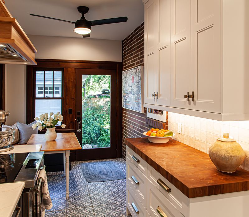 Dark woodwork, patterned terra cotta tile floors, and exposed brick interior walls define the kitchen and addition of this Craftsman home.