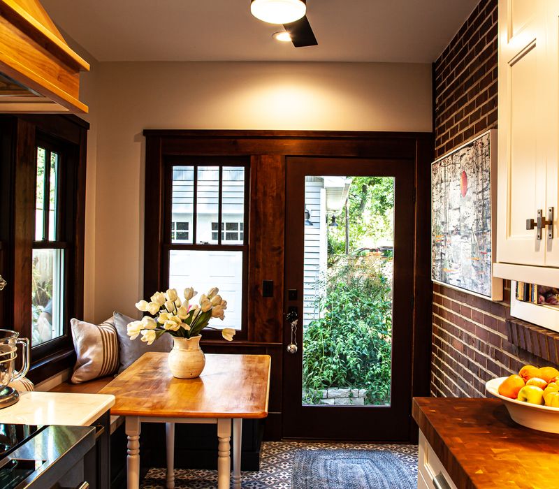 Dark woodwork, patterned terra cotta tile floors, and exposed brick interior walls define the kitchen and addition of this Craftsman home.