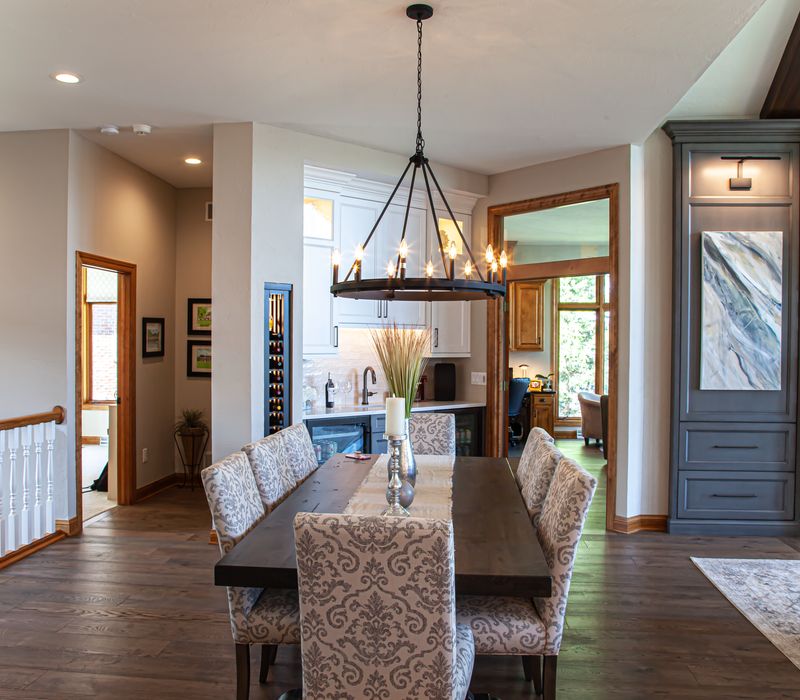 Gable end windows overlook the lake in this laid-back retreat featuring gray cabinetry, a black range hood with stainless steel accents, stone fireplaces, and wide plank wood floors. 