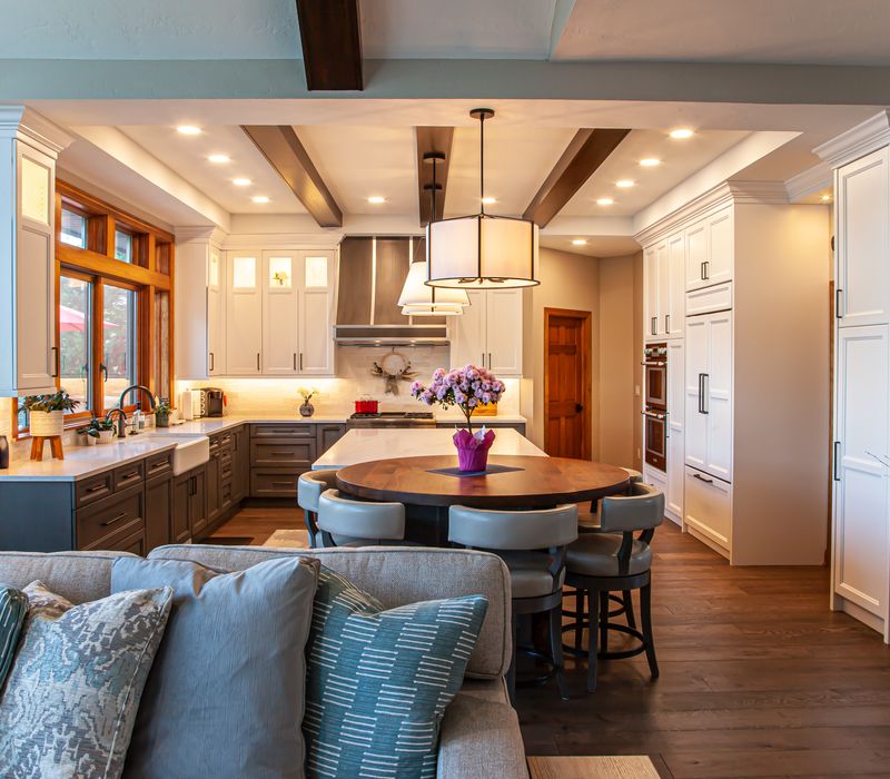 Gable end windows overlook the lake in this laid-back retreat featuring gray cabinetry, a black range hood with stainless steel accents, stone fireplaces, and wide plank wood floors. 