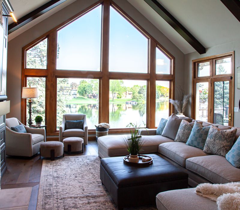 Gable end windows overlook the lake in this laid-back retreat featuring gray cabinetry, a black range hood with stainless steel accents, stone fireplaces, and wide plank wood floors. 