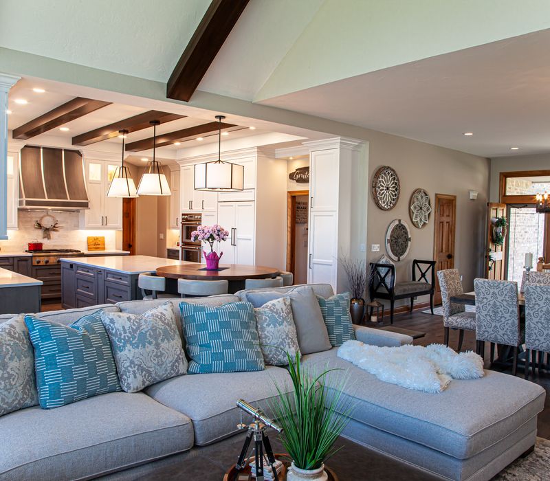 Gable end windows overlook the lake in this laid-back retreat featuring gray cabinetry, a black range hood with stainless steel accents, stone fireplaces, and wide plank wood floors. 