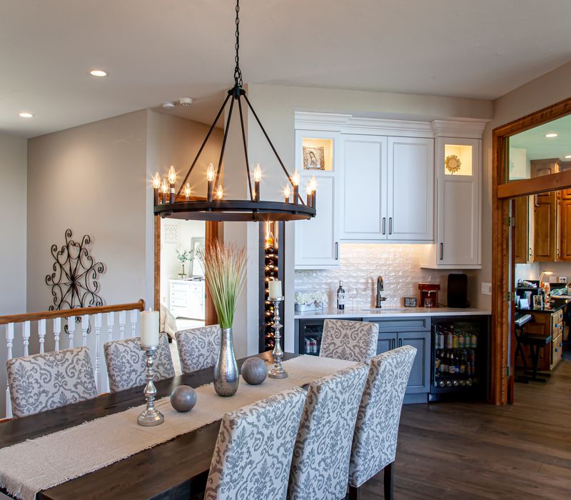 Gable end windows overlook the lake in this laid-back retreat featuring gray cabinetry, a black range hood with stainless steel accents, stone fireplaces, and wide plank wood floors. 