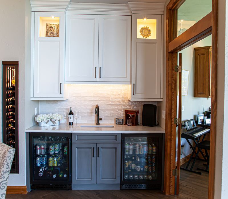 Gable end windows overlook the lake in this laid-back retreat featuring gray cabinetry, a black range hood with stainless steel accents, stone fireplaces, and wide plank wood floors. 