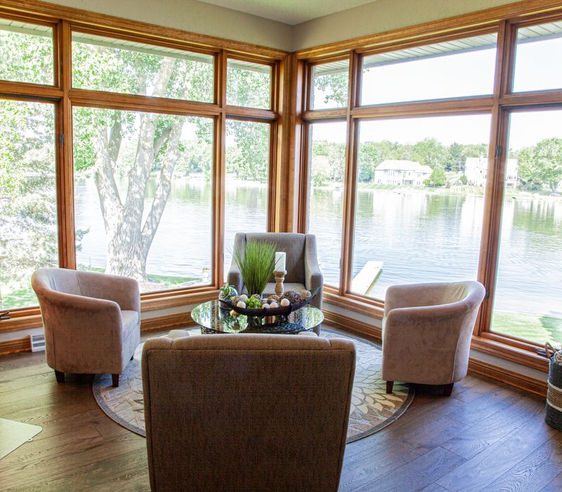 Gable end windows overlook the lake in this laid-back retreat featuring gray cabinetry, a black range hood with stainless steel accents, stone fireplaces, and wide plank wood floors. 