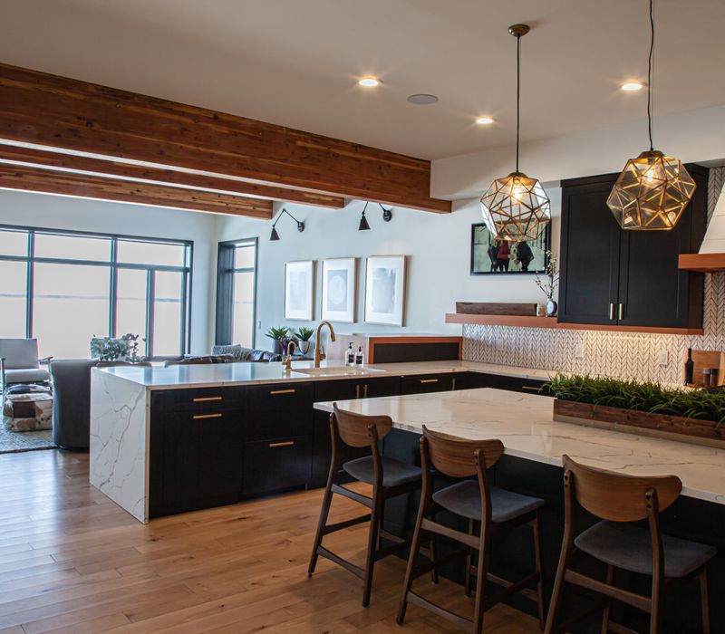 This mid-century modern home includes dramatic central stringer stairs behind a glass wall, white chevron tiles with dark grout, retro furniture, brushed gold fixtures, black cabinets, and laminated beams. 