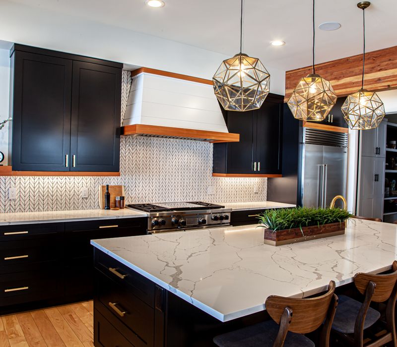 This mid-century modern home includes dramatic central stringer stairs behind a glass wall, white chevron tiles with dark grout, retro furniture, brushed gold fixtures, black cabinets, and laminated beams. 