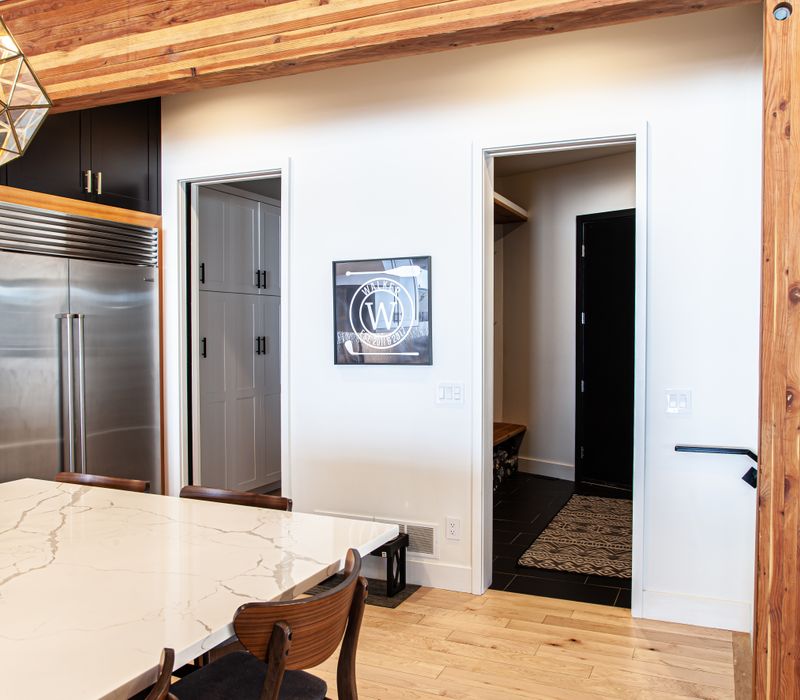 This mid-century modern home includes dramatic central stringer stairs behind a glass wall, white chevron tiles with dark grout, retro furniture, brushed gold fixtures, black cabinets, and laminated beams. 