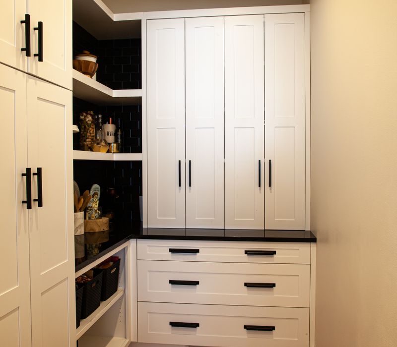This mid-century modern home includes dramatic central stringer stairs behind a glass wall, white chevron tiles with dark grout, retro furniture, brushed gold fixtures, black cabinets, and laminated beams. 