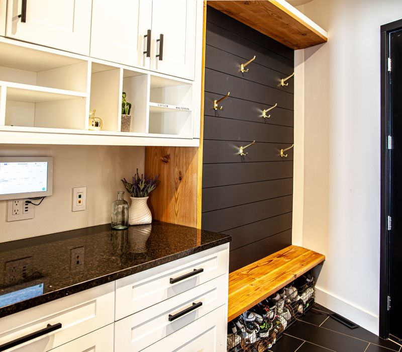 This mid-century modern home includes dramatic central stringer stairs behind a glass wall, white chevron tiles with dark grout, retro furniture, brushed gold fixtures, black cabinets, and laminated beams. 