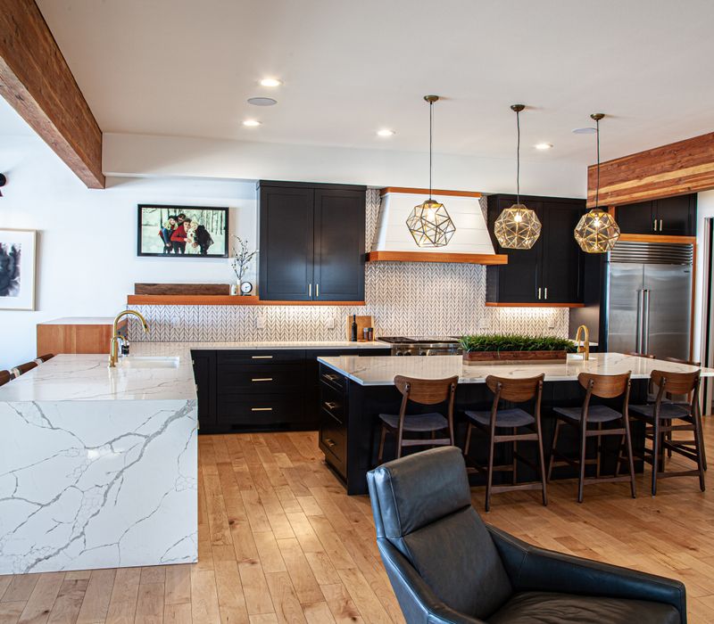 This mid-century modern home includes dramatic central stringer stairs behind a glass wall, white chevron tiles with dark grout, retro furniture, brushed gold fixtures, black cabinets, and laminated beams. 