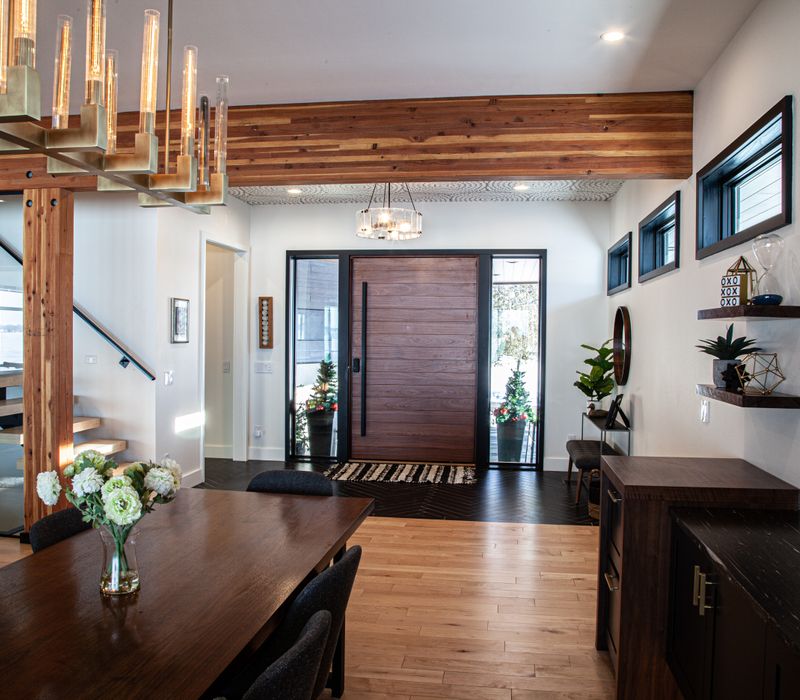 This mid-century modern home includes dramatic central stringer stairs behind a glass wall, white chevron tiles with dark grout, retro furniture, brushed gold fixtures, black cabinets, and laminated beams. 