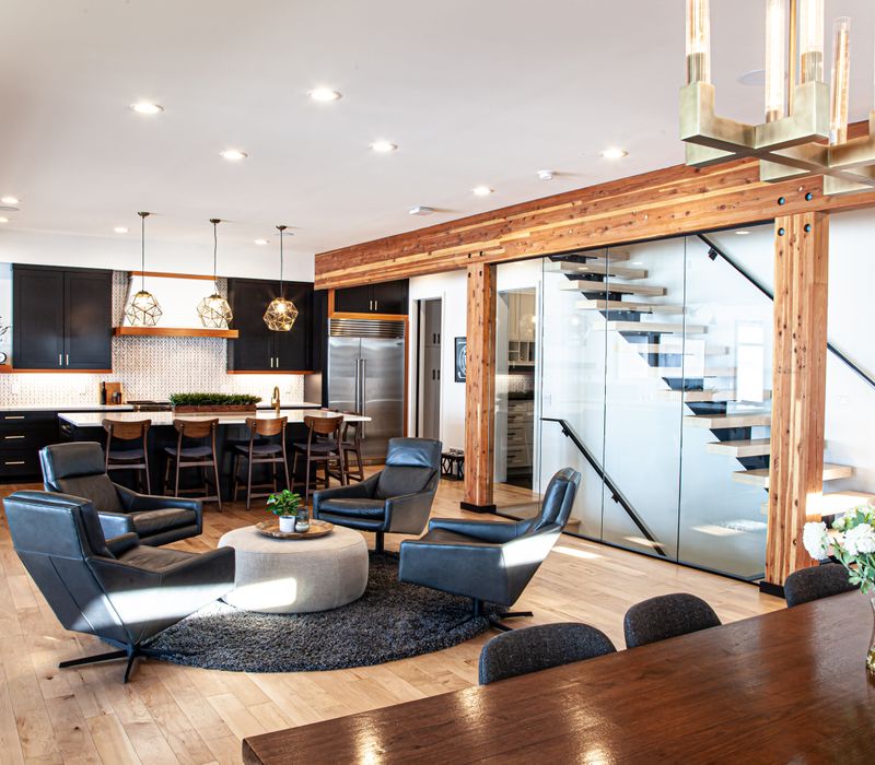 This mid-century modern home includes dramatic central stringer stairs behind a glass wall, white chevron tiles with dark grout, retro furniture, brushed gold fixtures, black cabinets, and laminated beams. 