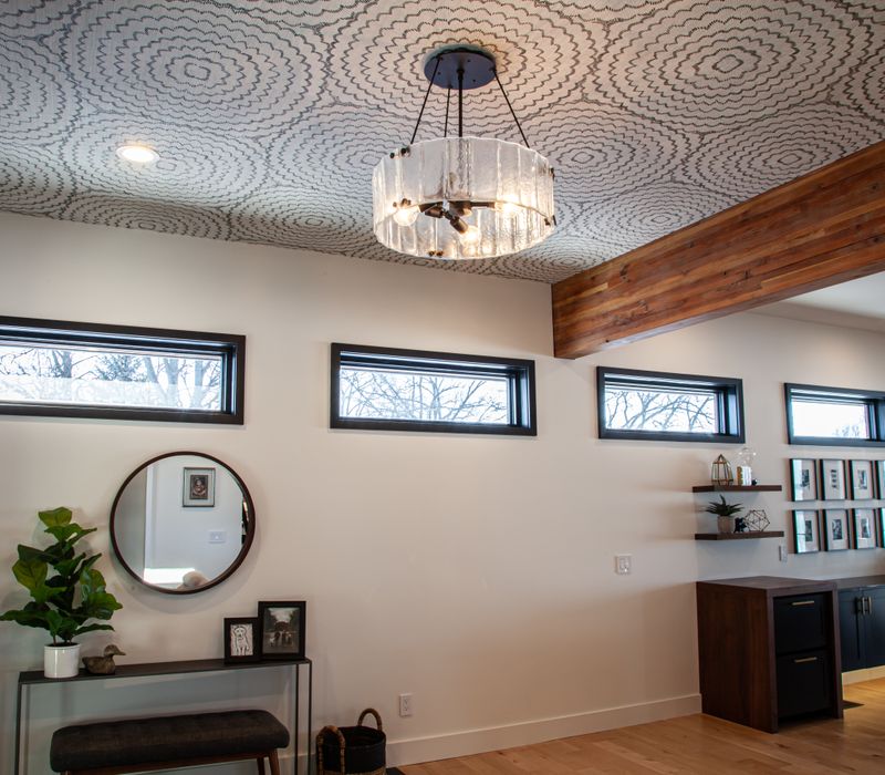 This mid-century modern home includes dramatic central stringer stairs behind a glass wall, white chevron tiles with dark grout, retro furniture, brushed gold fixtures, black cabinets, and laminated beams. 