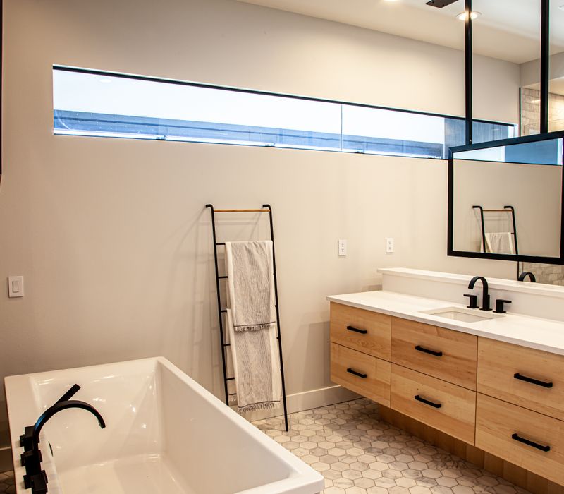 This mid-century modern home includes dramatic central stringer stairs behind a glass wall, white chevron tiles with dark grout, retro furniture, brushed gold fixtures, black cabinets, and laminated beams. 