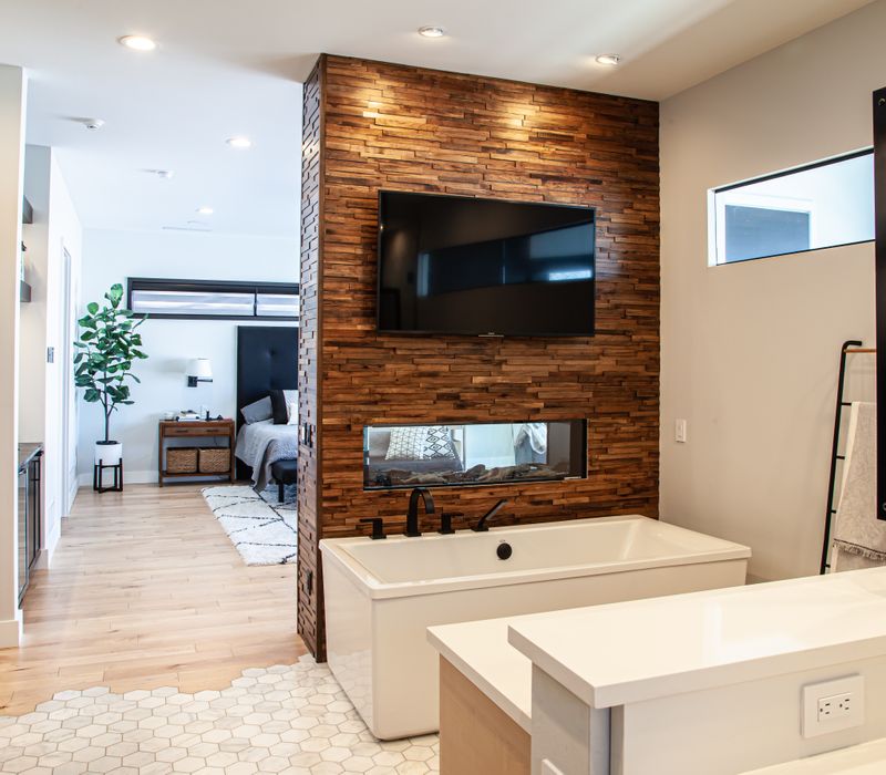 This mid-century modern home includes dramatic central stringer stairs behind a glass wall, white chevron tiles with dark grout, retro furniture, brushed gold fixtures, black cabinets, and laminated beams. 