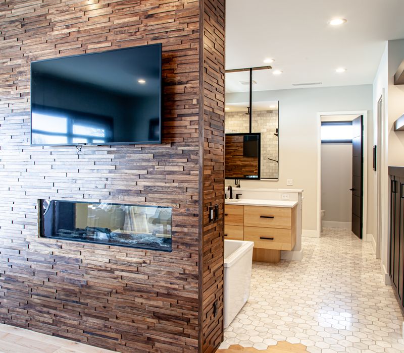 This mid-century modern home includes dramatic central stringer stairs behind a glass wall, white chevron tiles with dark grout, retro furniture, brushed gold fixtures, black cabinets, and laminated beams. 