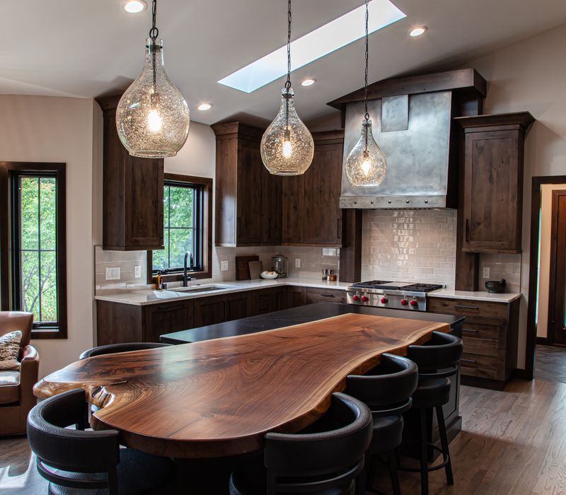 This house includes a brushed steel range hood, a live edge countertop, stone-seeded glass pendant lamps, skylights, and a barn door pantry. 