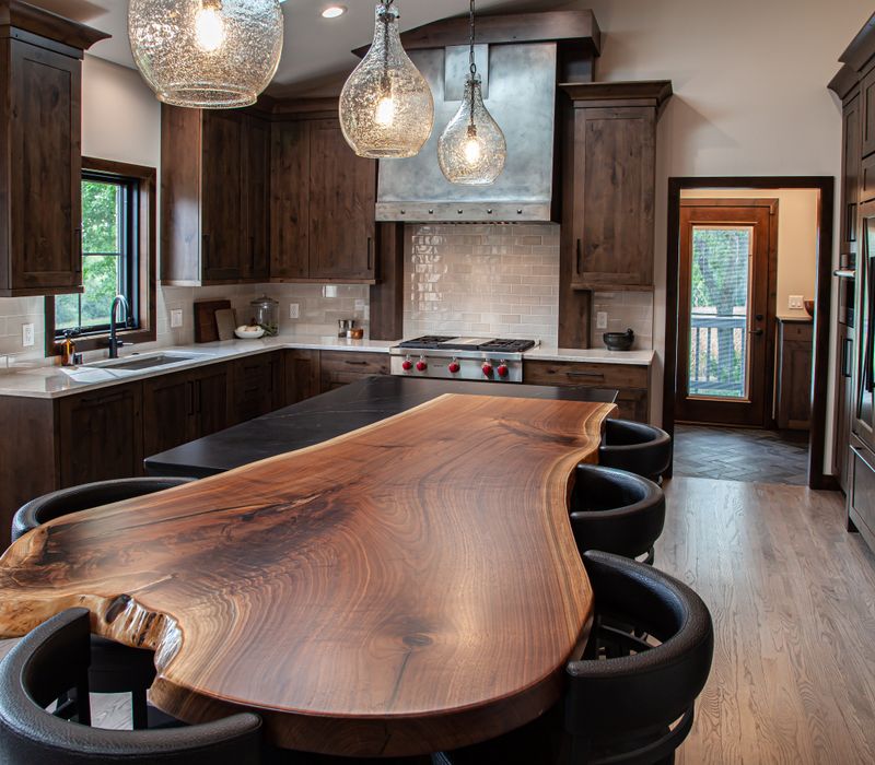 This house includes a brushed steel range hood, a live edge countertop, stone-seeded glass pendant lamps, skylights, and a barn door pantry. 