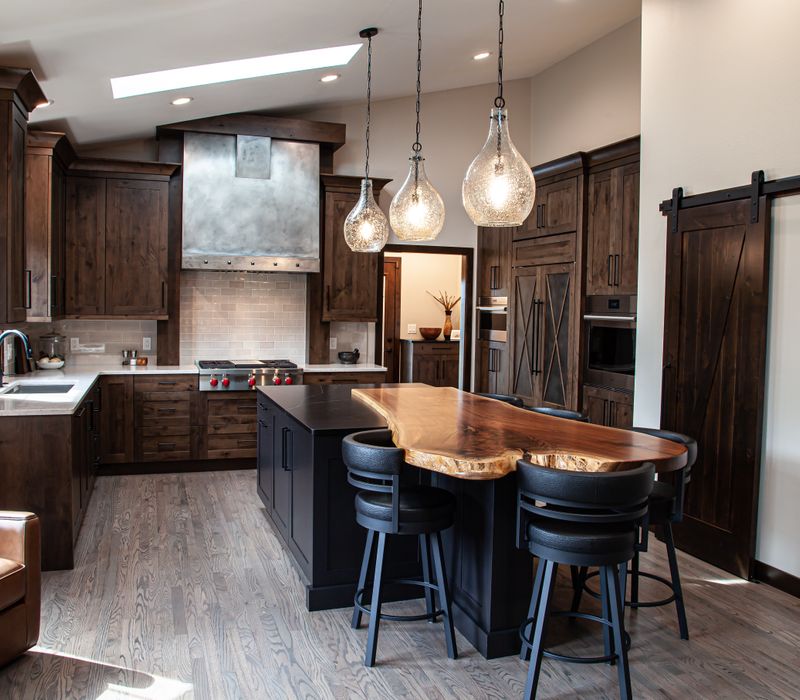 This house includes a brushed steel range hood, a live edge countertop, stone-seeded glass pendant lamps, skylights, and a barn door pantry. 