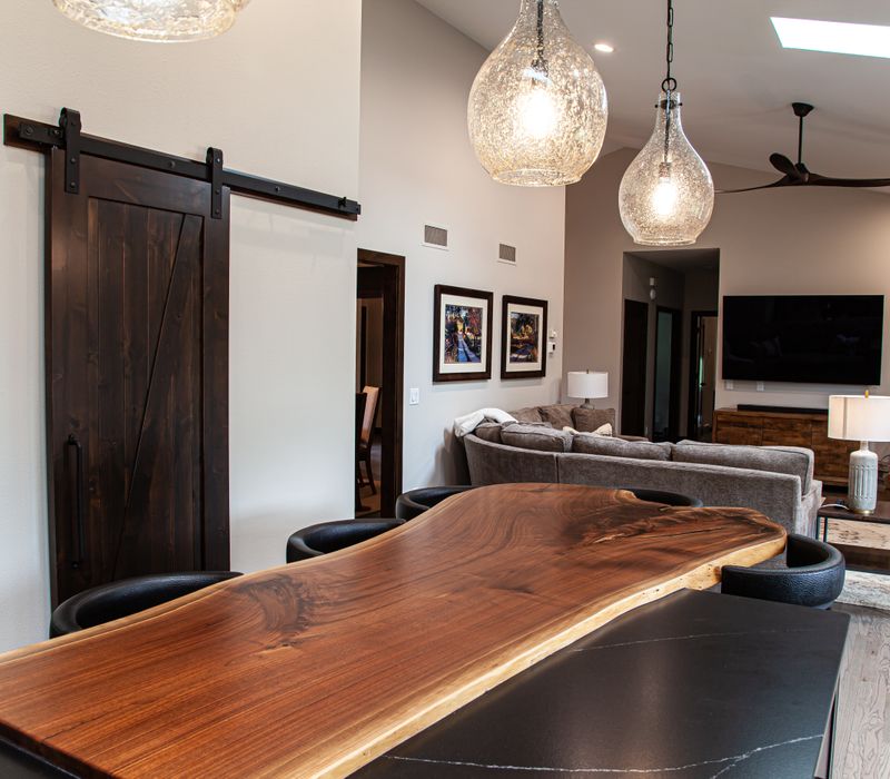 This house includes a brushed steel range hood, a live edge countertop, stone-seeded glass pendant lamps, skylights, and a barn door pantry. 