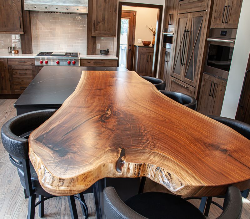 This house includes a brushed steel range hood, a live edge countertop, stone-seeded glass pendant lamps, skylights, and a barn door pantry. 
