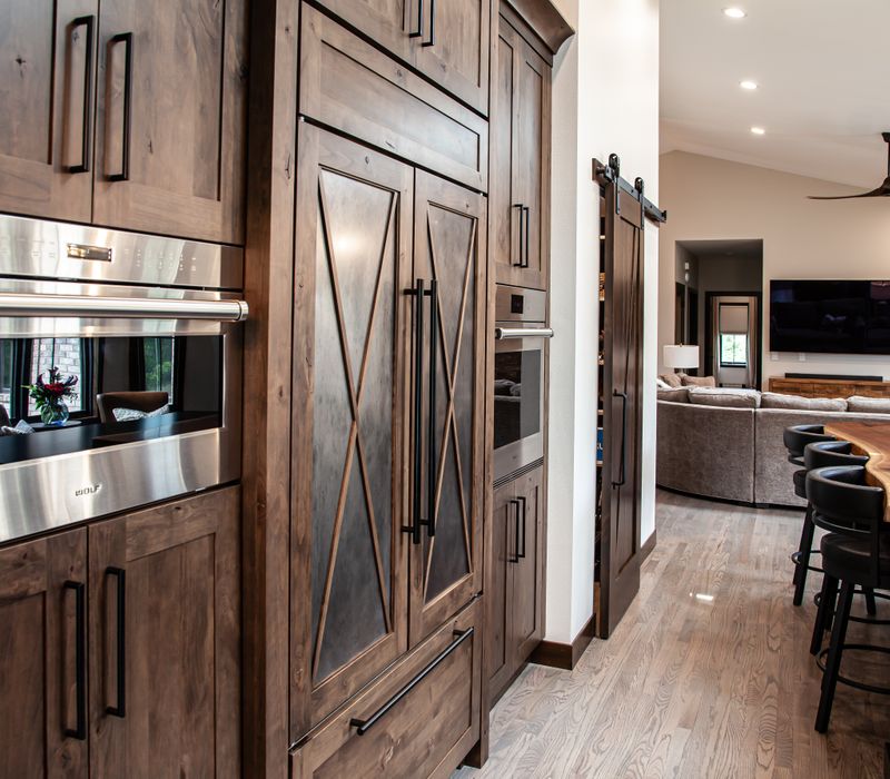 This house includes a brushed steel range hood, a live edge countertop, stone-seeded glass pendant lamps, skylights, and a barn door pantry. 