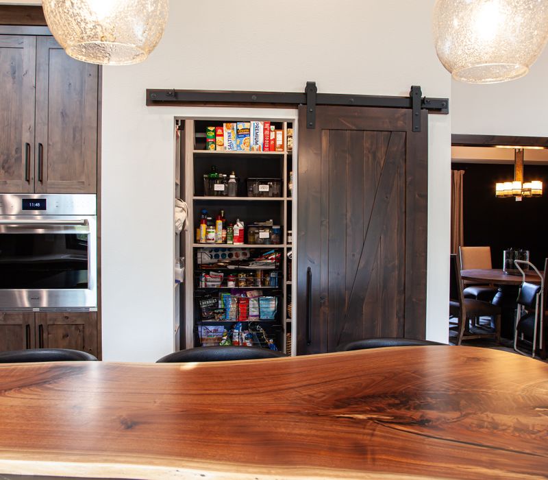 This house includes a brushed steel range hood, a live edge countertop, stone-seeded glass pendant lamps, skylights, and a barn door pantry. 