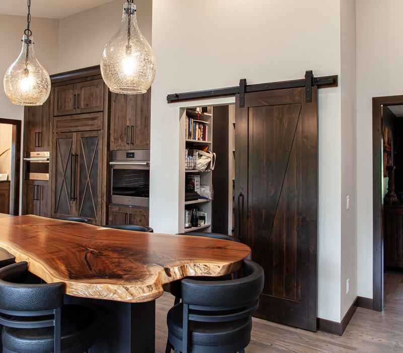This house includes a brushed steel range hood, a live edge countertop, stone-seeded glass pendant lamps, skylights, and a barn door pantry. 