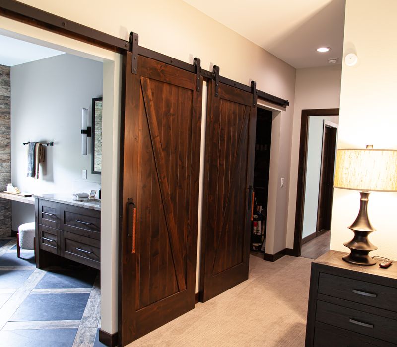 This house includes a brushed steel range hood, a live edge countertop, stone-seeded glass pendant lamps, skylights, and a barn door pantry. 