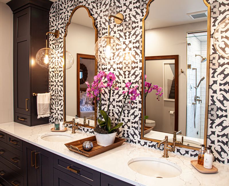Black and white encaustic tiles, gold-rimmed arch mirrors, and dark cabinetry give old world charm to this sumptuous bathroom.
