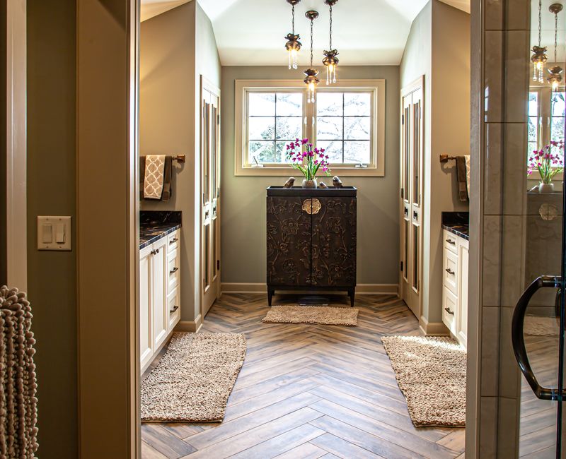 Bronze crosshatched mirror frames, herringbone wood look floor tile, and a vaulted ceiling add distinction to this two vanity bathroom.