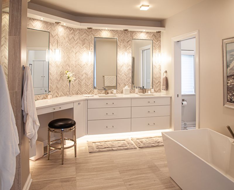 The neutral colors of the chevron wall tiles, spacious tiled walk-in shower, minimalist cabinetry, and a modern freestanding tub all set off the painting that is the centerpiece of this bathroom.