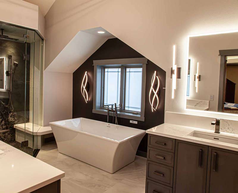 This bathroom features a freestanding tub in an alcove, set off by a dark accent wall with two modern sconces and a glass shower stall with a marble wall.