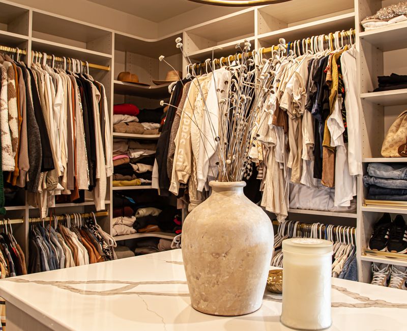 White cabinetry and shelving, a wood floor, and a gold chandelier add beauty to this functional walk-in closet that includes a washer and dryer.