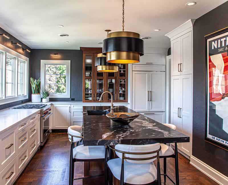 This complete kitchen remodel utilizes timeless materials, an intelligent reconfiguration of the space, and an effortless blend of natural light and warmth. It features cabinetry by DHDK, black quartzite countertops, herringbone wood flooring, a Broan pop-up downdraft hood, and a wet bar.