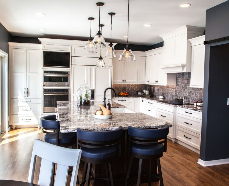 This kitchen combines patterned wall tile, stone countertops, Edison pendant lights, and elegant white cabinetry with a rustic barn door pantry and heavy wooden beams to define the space.