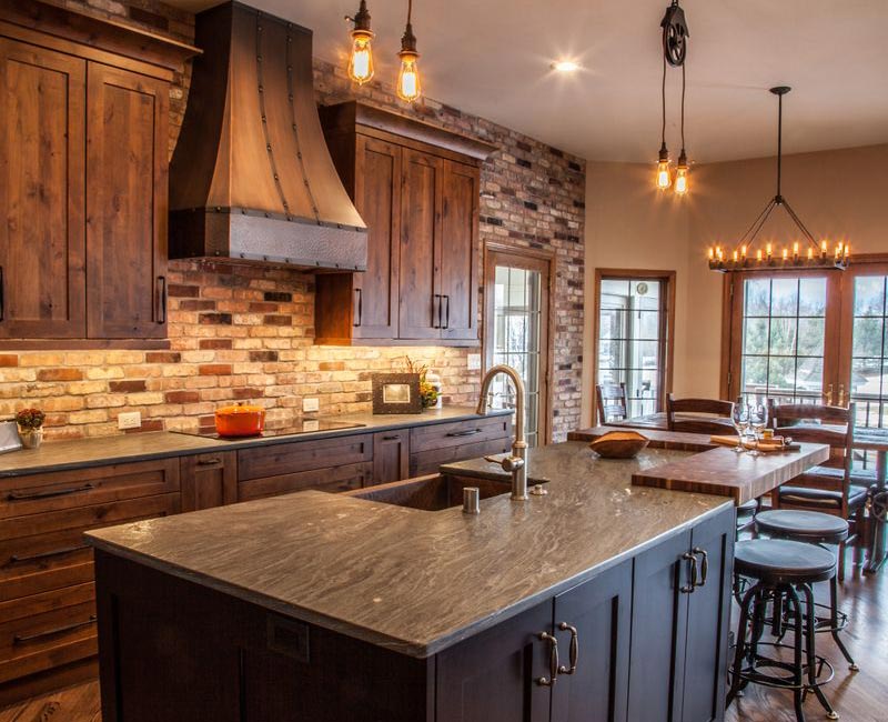 Rustic brick walls, rough-hewn beams, an end-grain cutting board, and a hammered copper sink and range hood add texture to this woodsy open concept kitchen.