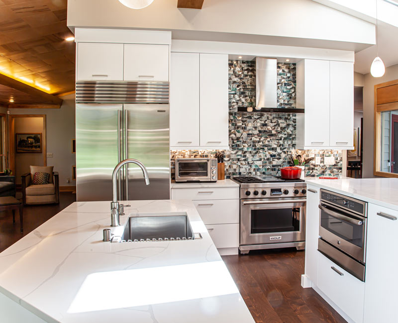 This kitchen remodel celebrates family, nature, and the unique geometry of the original home. It features crisp white cabinetry, cool-toned quartz countertops, two islands, and bold blue accents, plus a tactile mix of materials—wood, metal, glass, and stone—selected to stand the test of time in both durability and style.