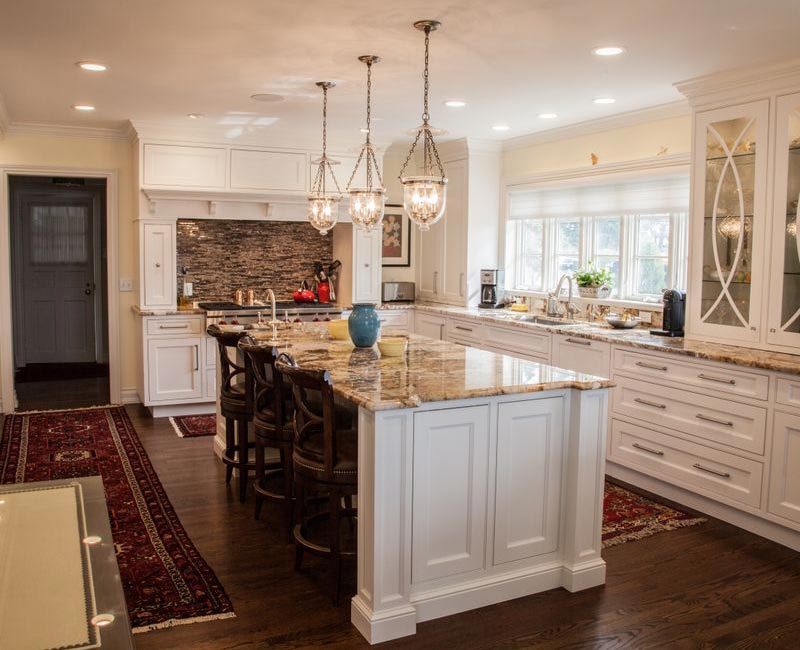Hardwood floors, polished stone countertops, a mosaic stone tile backsplash, white glass-front cabinetry, and glass pendant lanterns combine in this spacious kitchen.