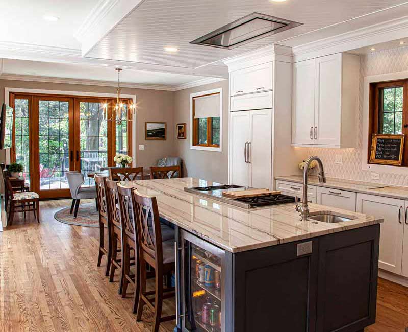 A kitchen featuring end-grain countertop, hardwood floors, and white glass tiles opens out onto a spacious deck in this Tudor style house.