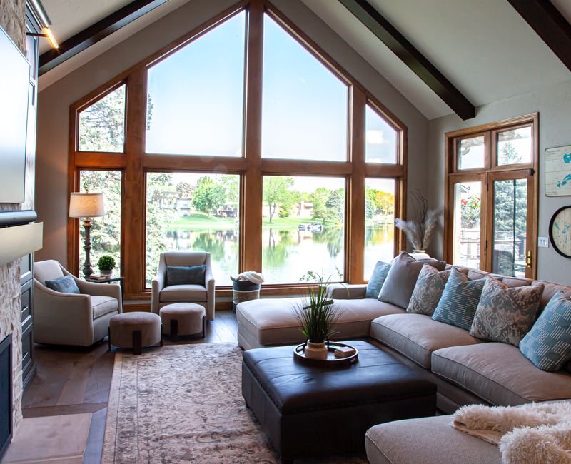 Gable end windows overlook the lake in this laid-back retreat featuring gray cabinetry, a black range hood with stainless steel accents, stone fireplaces, and wide plank wood floors. 