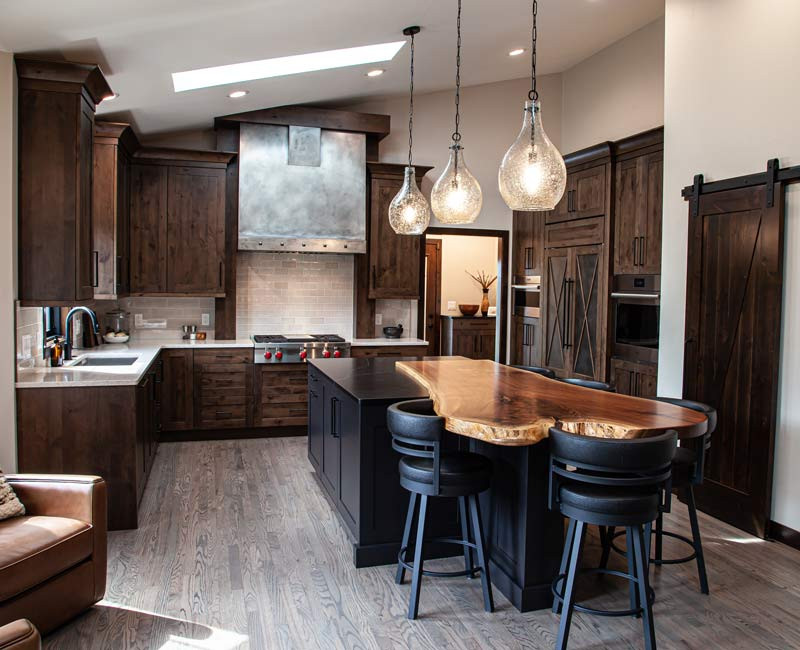 This house includes a brushed steel range hood, a live edge countertop, stone-seeded glass pendant lamps, skylights, and a barn door pantry. 